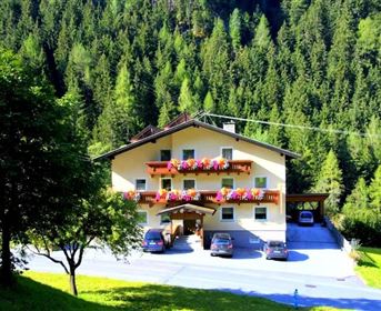 Ein gemütliches Haus inmitten eines schönen Waldes. Es hat blühende Balkone und ist von Bäumen umgeben.