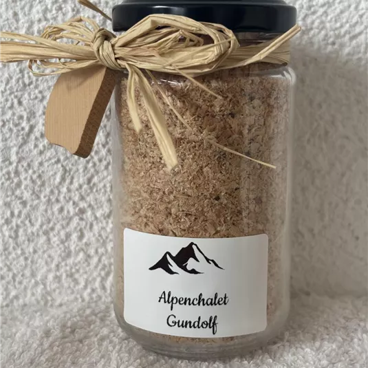 Ein Glas mit einem Deckel, gefüllt mit braunem Inhalt, das mit Jute-Schnur dekoriert ist. Auf dem Etikett steht "Alpenchalet Gundolff".