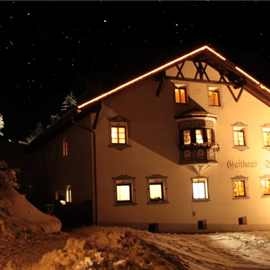 A charming, illuminated house in the snow at night. The clear starry sky and the snow-covered trees create a tranquil winter atmosphere.
