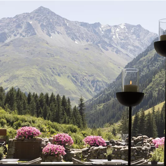 Eine beeindruckende Berglandschaft mit grünen Wiesen und blühenden Blumen. Im Vordergrund sind Kerzenhalter zu sehen, die eine entspannende Atmosphäre schaffen.