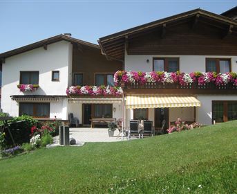 Ein gemütliches Haus mit einem schönen Garten und blühenden Pflanzen. Die Balkone sind mit bunten Blumen geschmückt.