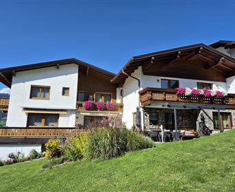Ein schönes Haus mit einem großen Garten und bunten Blumen. Der Himmel ist klar und blau, was die friedliche Atmosphäre verstärkt.