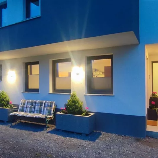 Ein modernes Haus mit einem einladenden Eingangsbereich. Draußen steht eine Sitzbank und es sind kleine Pflanzen dekorativ angeordnet.