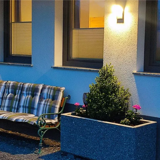 Eine gemütliche Bank steht vor einem Haus mit blauen Wänden. Zwei Pflanzkästen mit Blumen sorgen für eine einladende Atmosphäre.