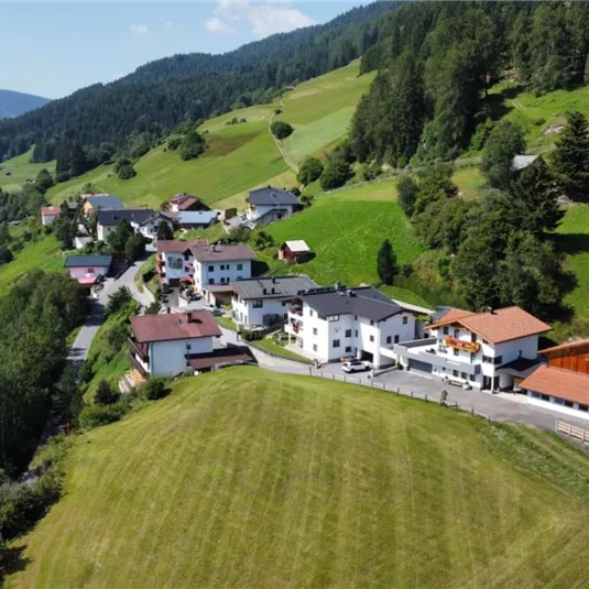 Ein malerisches Dorf in grüner Landschaft mit Häusern und Wiesen. Im Hintergrund sind sanfte Hügel und Wälder zu sehen.