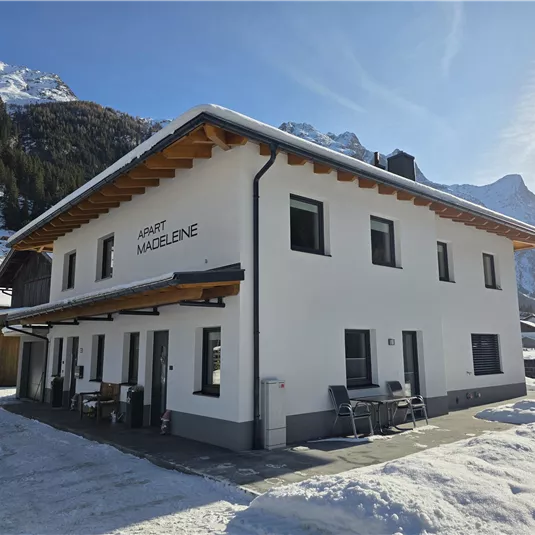 Ein modernes Gebäude im Schnee mit Bergblick. Die Fassade ist hell und hat große Fenster.