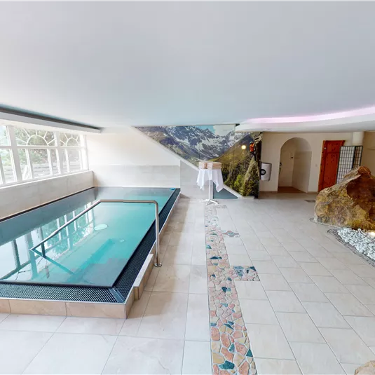 Ein eleganter Wellnessbereich mit einem modernen Pool und natürlichem Licht. Die entspannende Atmosphäre wird durch Felsen und sanfte Farben unterstrichen.