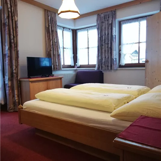 Ein gemütliches Schlafzimmer mit zwei Betten und frischen Bettdecken. Es gibt einen Fernseher und große Fenster, die viel Licht hereinlassen.