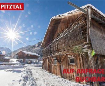 A snowy landscape with traditional wooden houses in the Pitztal. The sun shines brightly over the mountains.