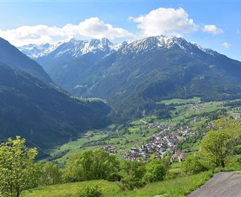 A picturesque mountain landscape with snow-capped peaks and green valleys. In the foreground, there is a small village.