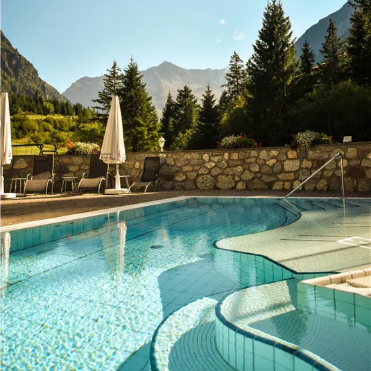 Ein klarer Pool umgeben von Bergen und Bäumen. Entspannte Liegen stehen bereit, um die Aussicht zu genießen.