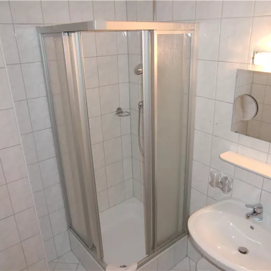 A modern bathroom with a shower stall and a sink. The walls are tiled with white tiles.