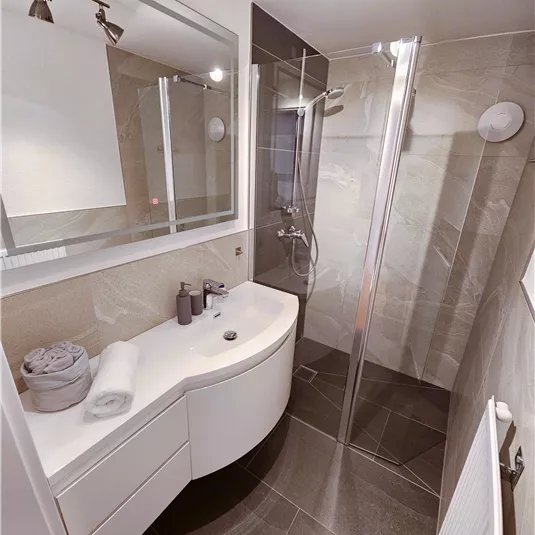Ein modernes Badezimmer mit eleganter Dusche und stilvollem Waschbecken. Die Wände sind hell gefliest und schaffen eine angenehme Atmosphäre.