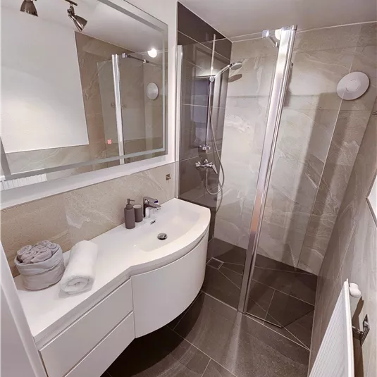 A modern bathroom with an elegant shower and stylish sink. The walls are light tiled, creating a pleasant atmosphere.