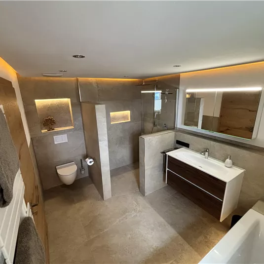 Ein modernes Badezimmer mit eleganten, grauen Wänden und warmem Licht. Es gibt eine Dusche, eine Badewanne und einen stilvollen Schrank.