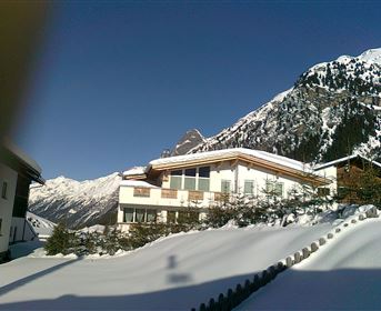 Eine moderne Berghütte im Schnee mit schneebedeckten Bergen im Hintergrund. Die klare Himmel und die besondere Berglandschaft schaffen eine idyllische Winteratmosphäre.