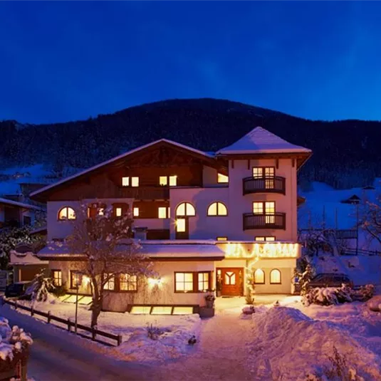 A cozy hotel in the snow at night. The brightly lit windows radiate warmth into the winter landscape.