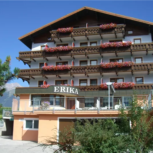 A charming hotel named "ERIKA" with several balconies adorned with flowers. In the background, a clear blue sky can be seen.