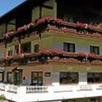 A cozy hotel with balconies adorned with flowers. In the background, green mountains can be seen.