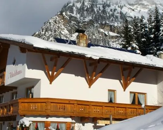 Ein charmantes, snow-bedecktes Hotel mit Holzverkleidung in den Alpen. Im Hintergrund sind majestätische Berge und blauer Himmel zu sehen.