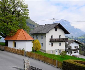Eine malerische Berglandschaft mit zwei hübschen Häusern und einem kleinen Pavillon. Bäume und eine grüne Wiese schaffen eine ruhige Atmosphäre.