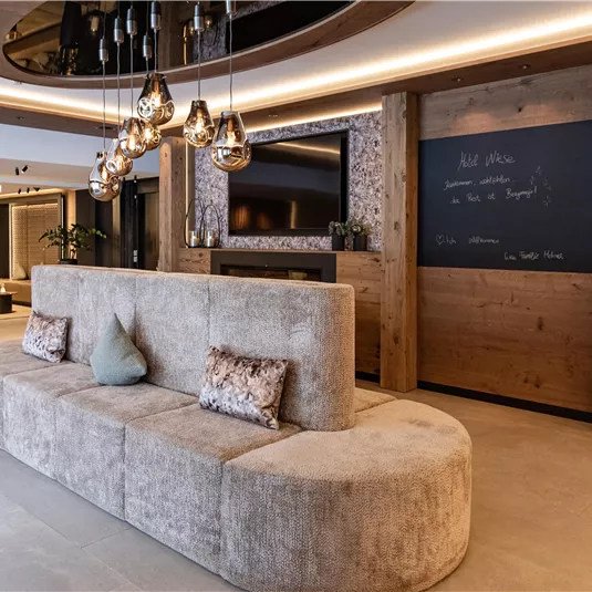 A modernly designed living area with a beige, curved sofa and warm light. On the wall, there is a board inviting you to write.