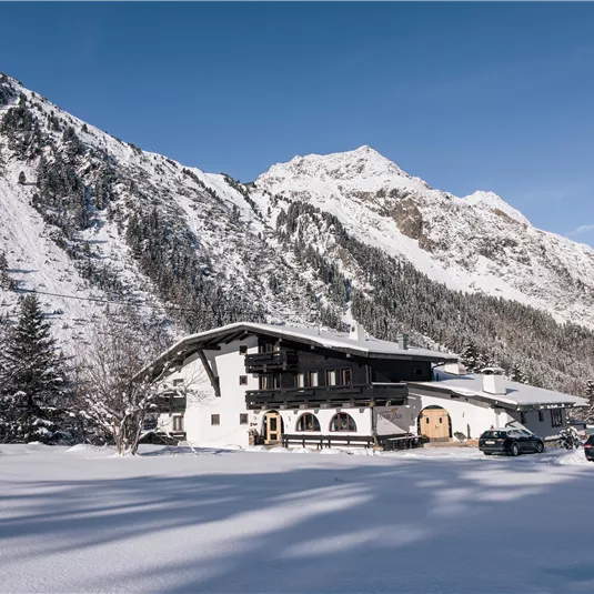 Ein schönes Berghaus in einer schneebedeckten Landschaft. Im Hintergrund sind majestätische Berge unter blauem Himmel zu sehen.