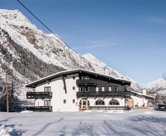 Ein charmantes Haus im Schnee, umgeben von majestätischen Bergen. Der klare blaue Himmel vervollständigt die winterliche Landschaft.
