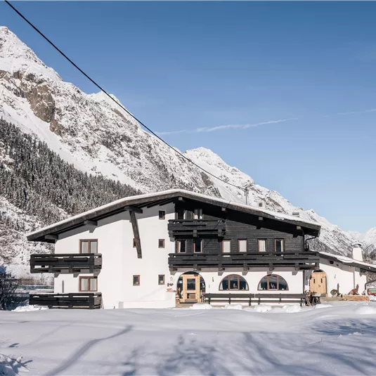 Ein charmantes Haus im Schnee, umgeben von majestätischen Bergen. Der klare blaue Himmel vervollständigt die winterliche Landschaft.