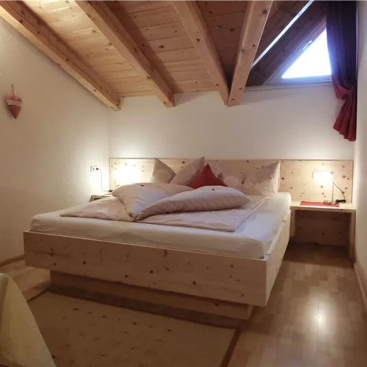 Ein gemütliches Schlafzimmer mit einem großen Doppelbett und Holzvertäfelung. Sanfte Beleuchtung und ein Fenster sorgen für eine entspannte Atmosphäre.
