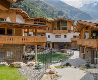 Eine elegante Almhütte mit Holzbalkonen und Naturstein. Im Hintergrund sind beeindruckende Berge und ein gepflegter Garten zu sehen.