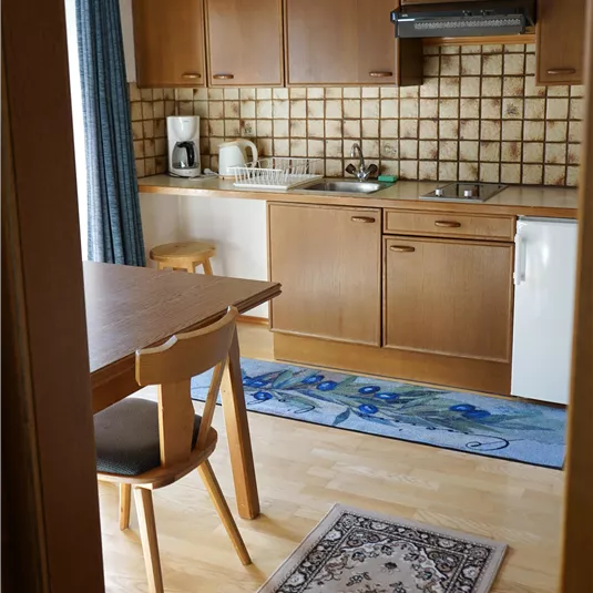 Eine gemütliche Küche mit Holzschränken und einem kleinen Tisch. Der Boden ist mit einem Teppich und einem blauen Läufer dekoriert.