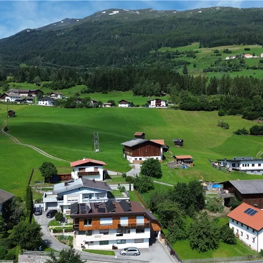 A picturesque village amidst green meadows and gentle hills. The houses are surrounded by magnificent nature and mountains in the background.