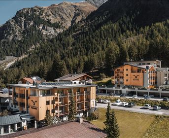 Eine malerische Alpenlandschaft mit modernen Hotels und grünen Wäldern. Die Berge im Hintergrund verleihen der Szenerie eine beeindruckende Kulisse.
