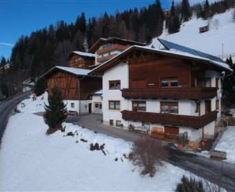A cozy wooden house in the snow, surrounded by mountains and fir trees. The path runs right next to the building.