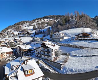 A snowy landscape with charming houses and a blue sky. Gentle hills surround the village, which is wrapped in winter blankets.