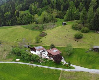 Ein malerisches Bauernhaus liegt zwischen sanften Hügeln und saftigem Grün. Die Umgebung ist geprägt von Wäldern und einer ruhigen Straße.