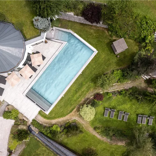 A stylish outdoor area with a sparkling pool and well-maintained greenery. Surrounded by trees and loungers, the area offers a place to relax.