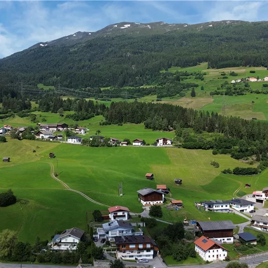 A picturesque landscape with green meadows and a small village in the valley. In the background, mountains and a blue sky can be seen.