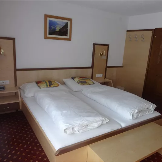 A simple hotel room with two single beds and wooden decor. A picture hangs on the wall, and there is a table as well as a chair.