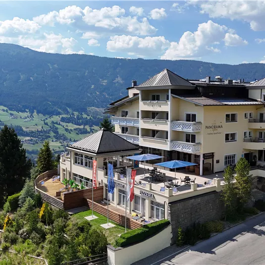 Ein modernes Hotel in den Bergen mit einer schönen Terrasse und Blick auf das Tal. Umgeben von Bäumen und einer malerischen Landschaft.