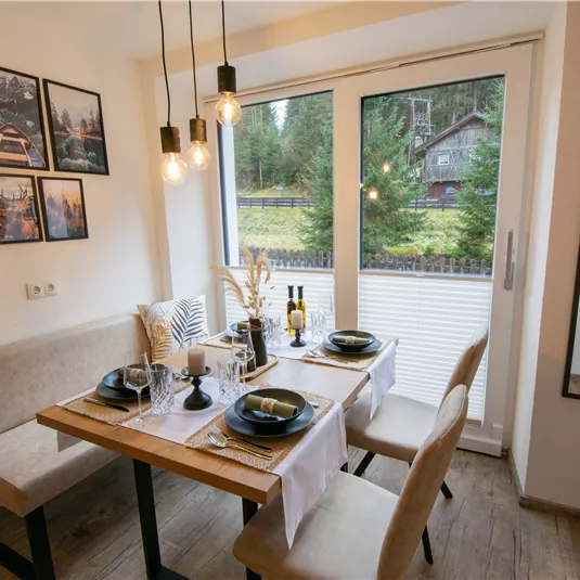 An inviting dining area with a wooden table and cozy benches. Large windows provide a view of the surroundings and allow plenty of natural light in.