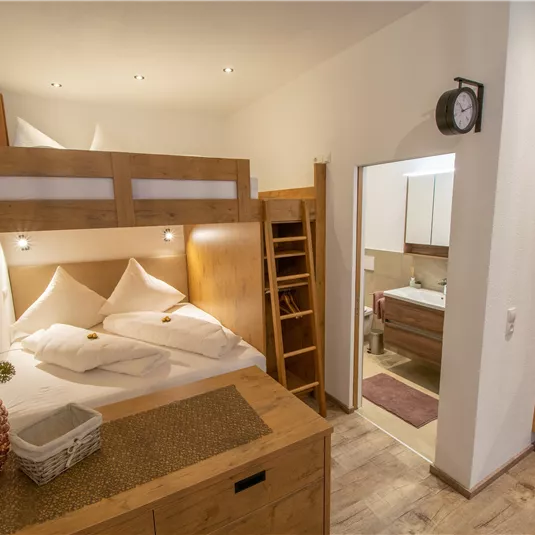 A cozy room with a double bed, wooden shelves, and a modern bathroom. The decor is bright and friendly.