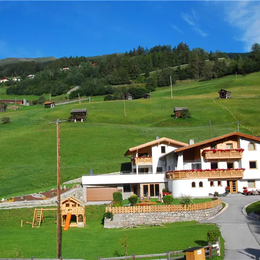 Ein schönes Haus in einer grünen Hügellandschaft. Die Umgebung ist ruhig und friedlich, mit blauen Himmel und wenigen Wolken.