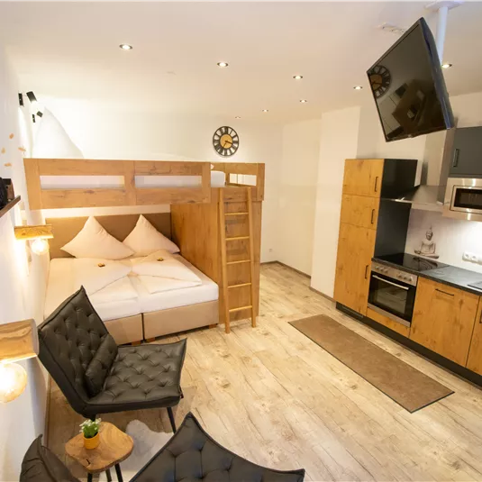 A modern living kitchen with a cozy bedroom area. The room features wooden furniture and a television on the wall.