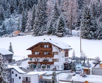 Ein schönes, schneebedecktes Haus umgeben von Tannenbäumen. Die Landschaft zeigt eine ruhige, winterliche Atmosphäre.