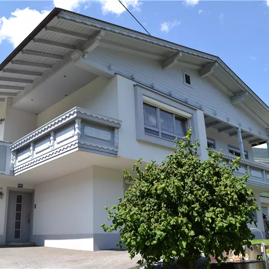 A modern house with a large balcony and light paint. Surrounded by greenery and a beautiful landscape.