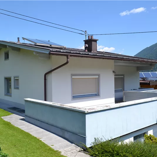 A modern house with a flat roof and solar panels. It is located in a picturesque landscape with mountains in the background.