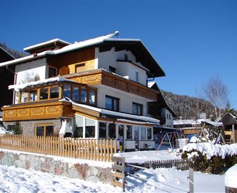 A beautiful house in the snow with wooden elements and a surrounding balcony. The surroundings are wintry and peaceful.