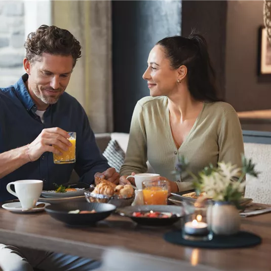 A couple is sitting at a table in a cozy café. They are enjoying their breakfast and smiling at each other.